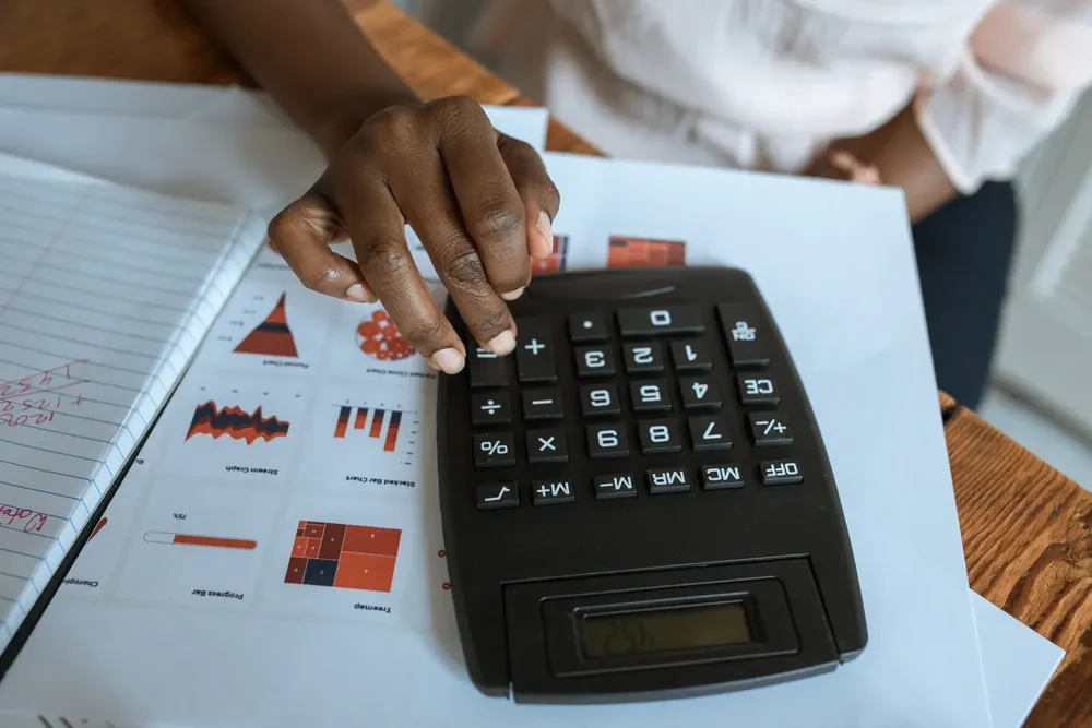A hand using a calculator on a desk with printed charts