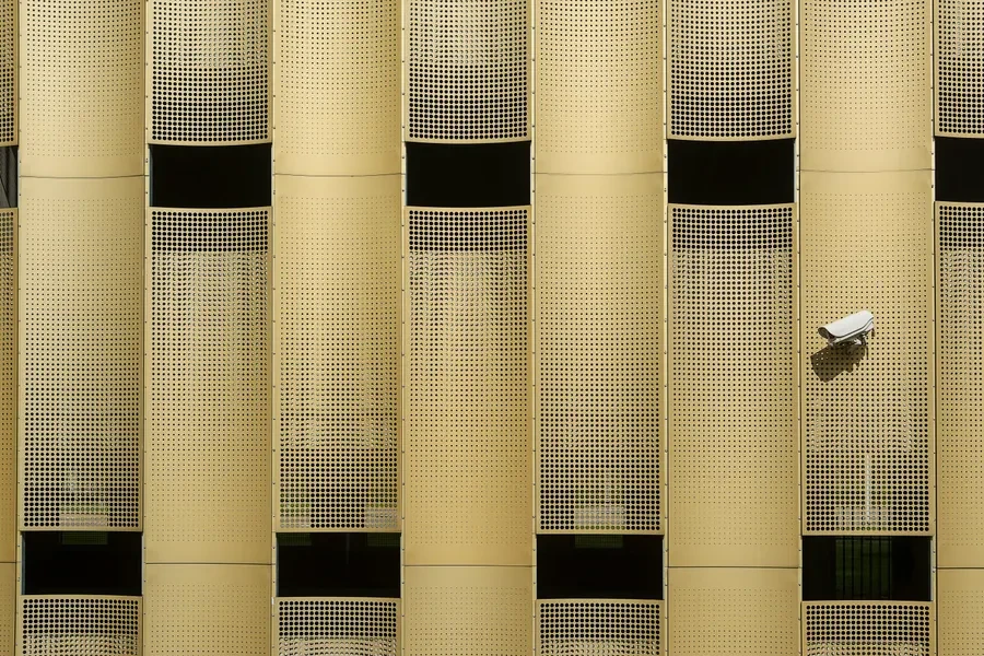 A fixed security camera on a building facade clad in perforated metal panels